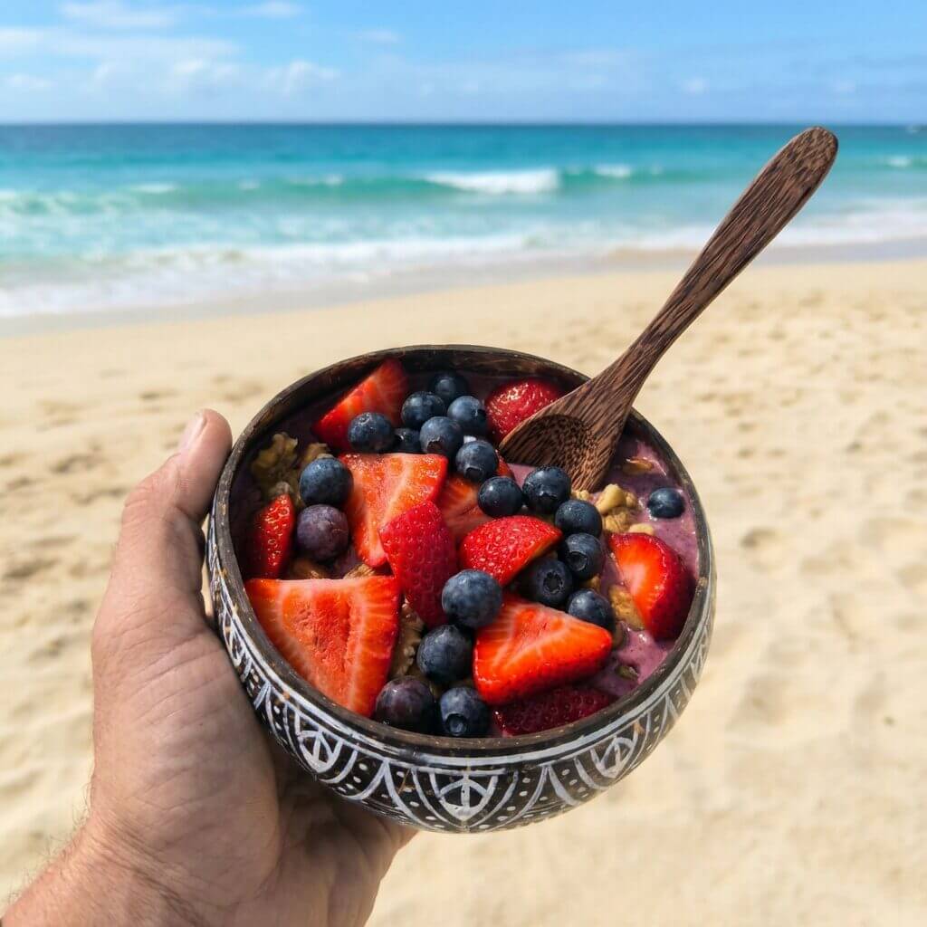 Acai Bowl von einer männlichen Hand gehalten am Strand